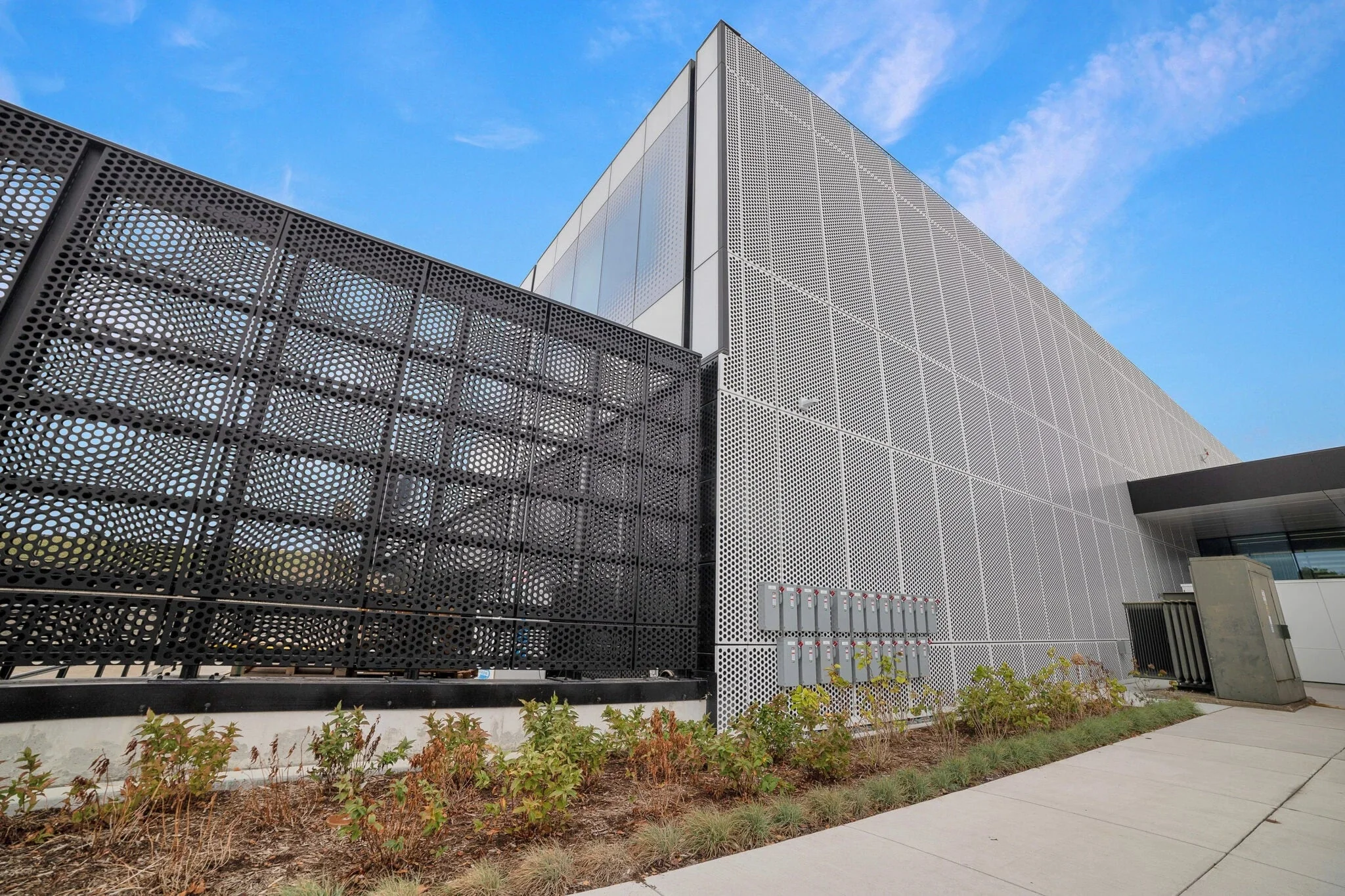 Perforated stainless steel architectural facade panel, afternoon light showing controlled open area pattern.