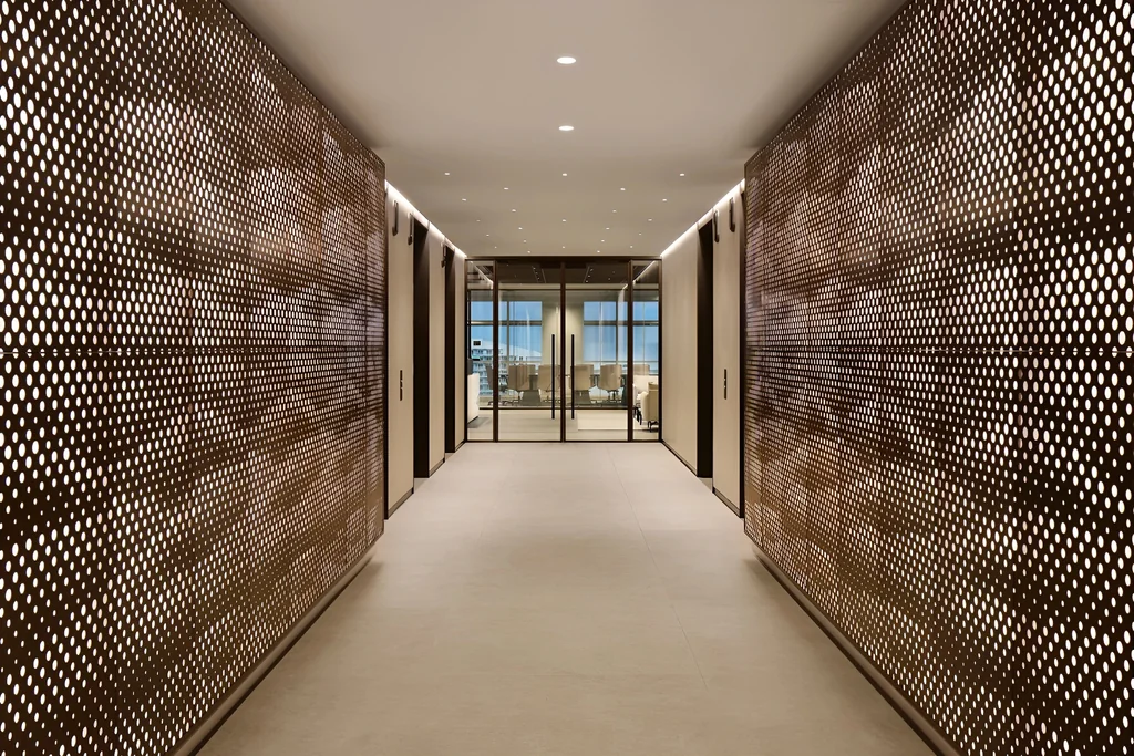 Bronze perforated metal screen walls lining a corridor in a Shenzhen tech office, leading to a glass-walled meeting room